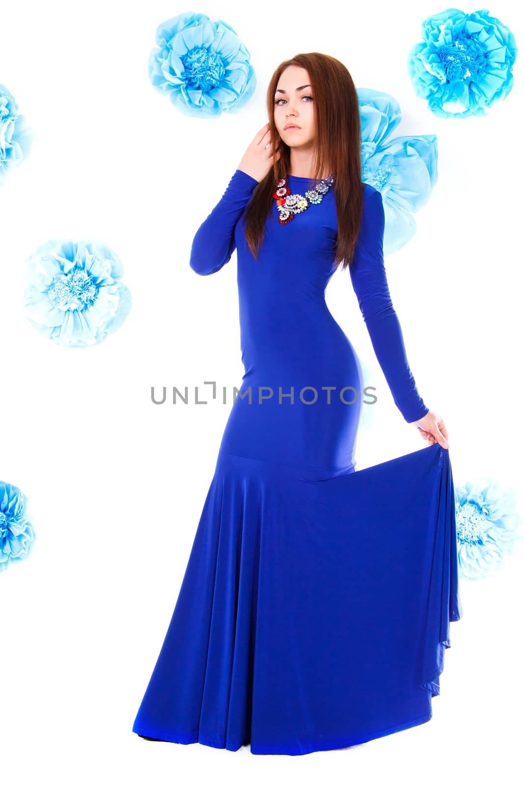 Beautiful young woman in a long blue evening dress at the background of the cyan flowers