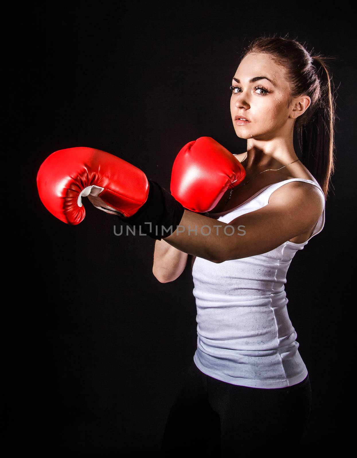 Beautiful young woman in a red boxing gloves over black background