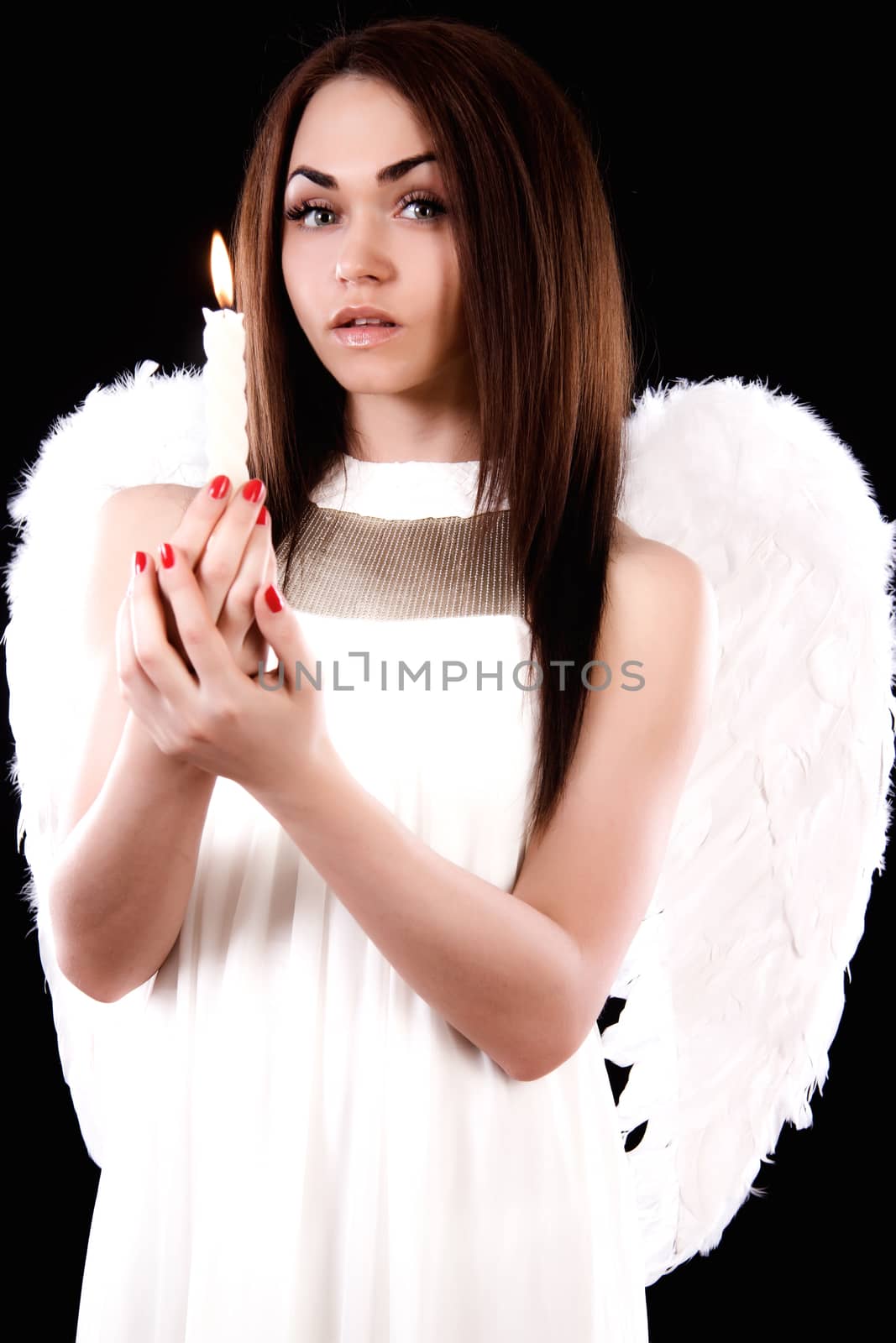 Beautiful young angel holding a candle over black background