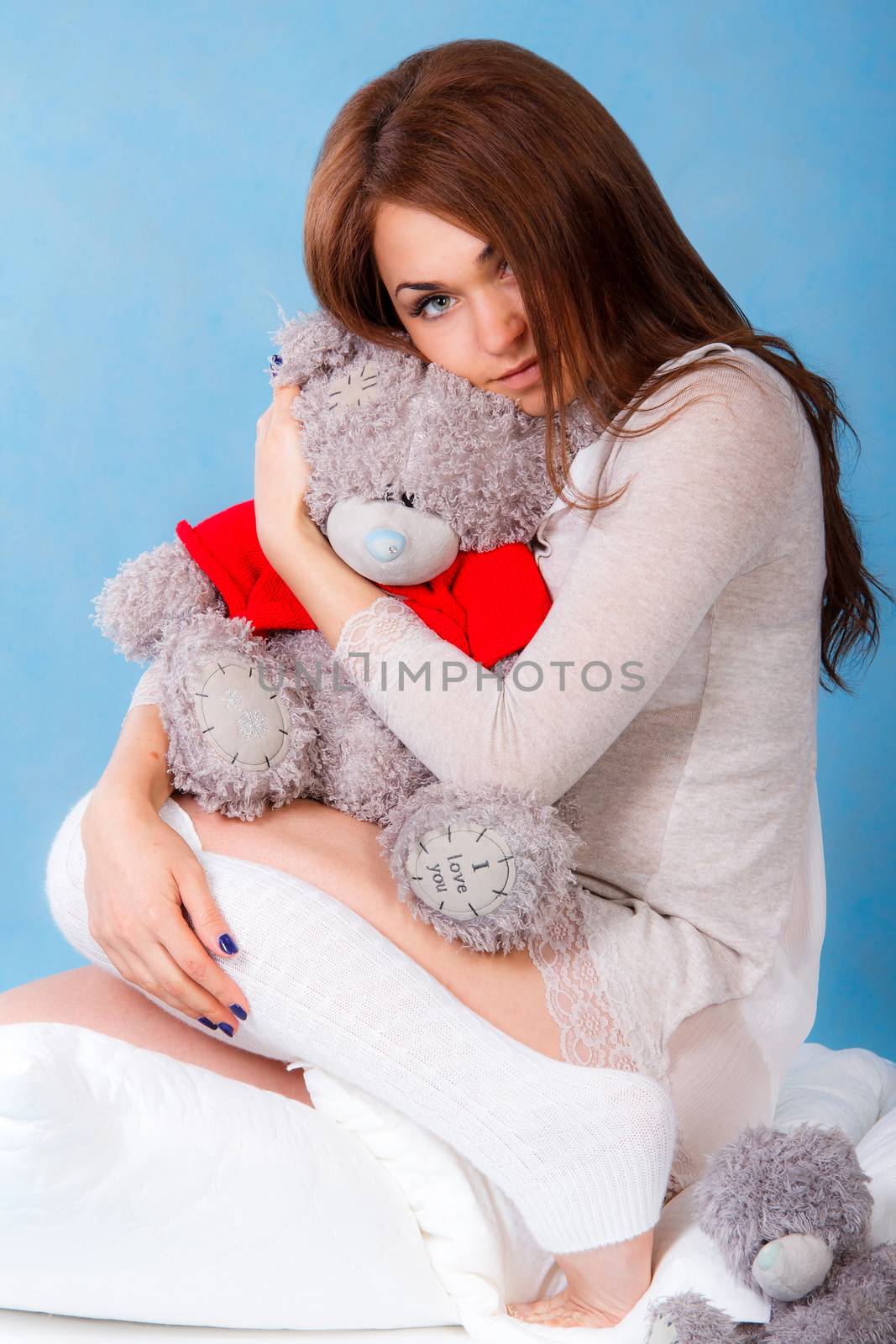 Beautiful young woman with teddy bear in a bed over blue background