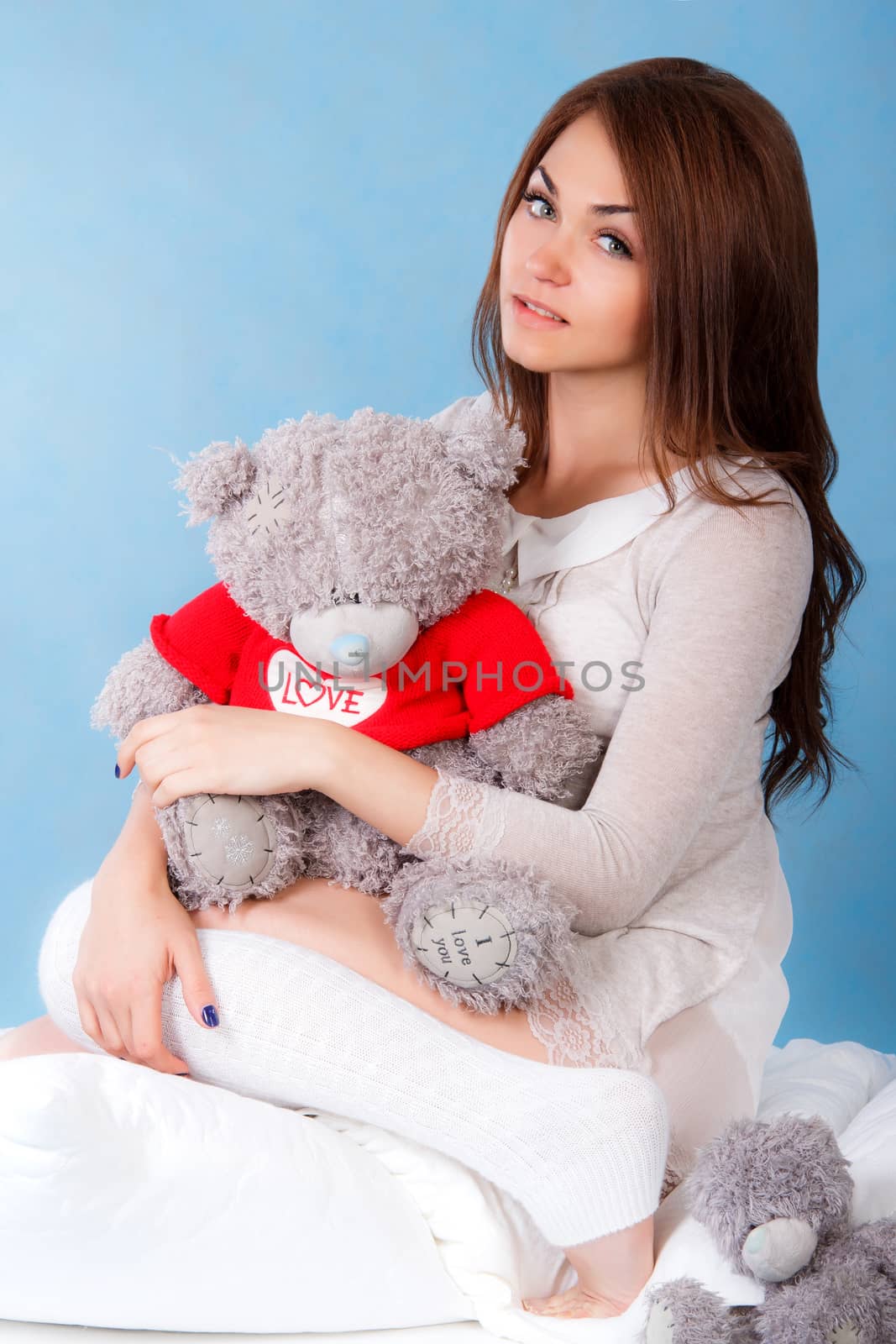 Beautiful young woman with teddy bear in a bed over blue background