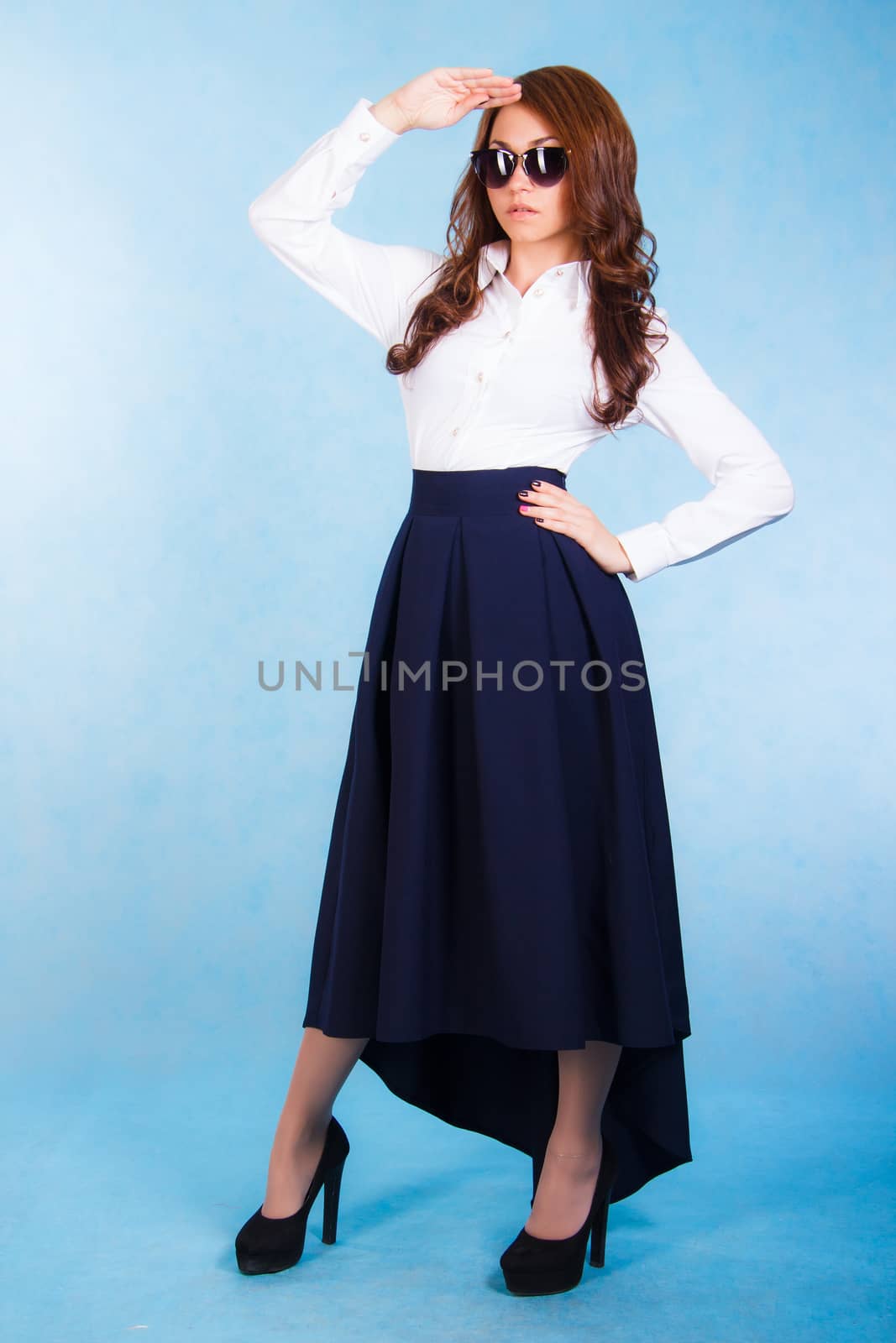 Beautiful young woman in a white shirt and a long blue skirt over cyan background