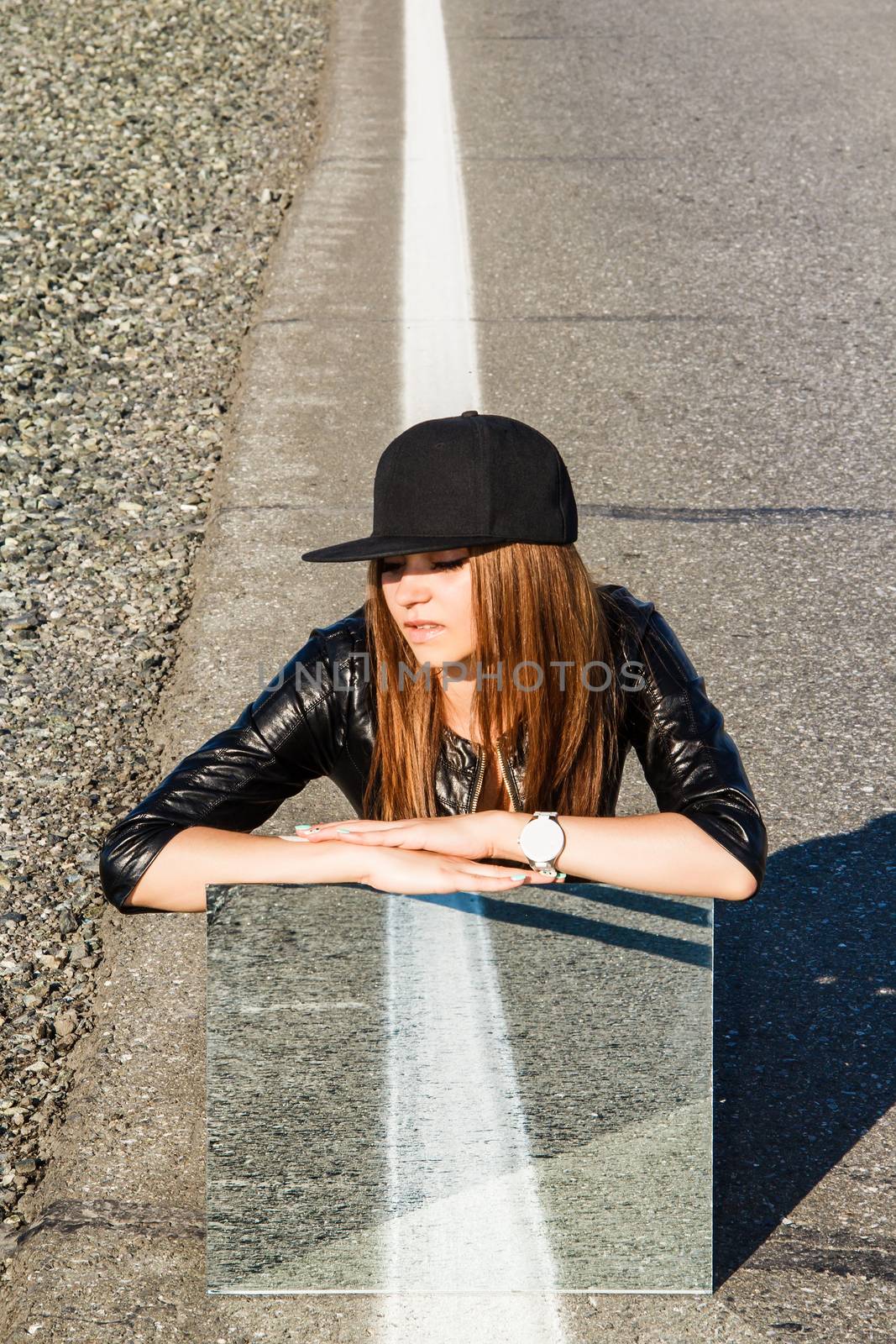 Beautiful young woman sitting on the road with a mirror