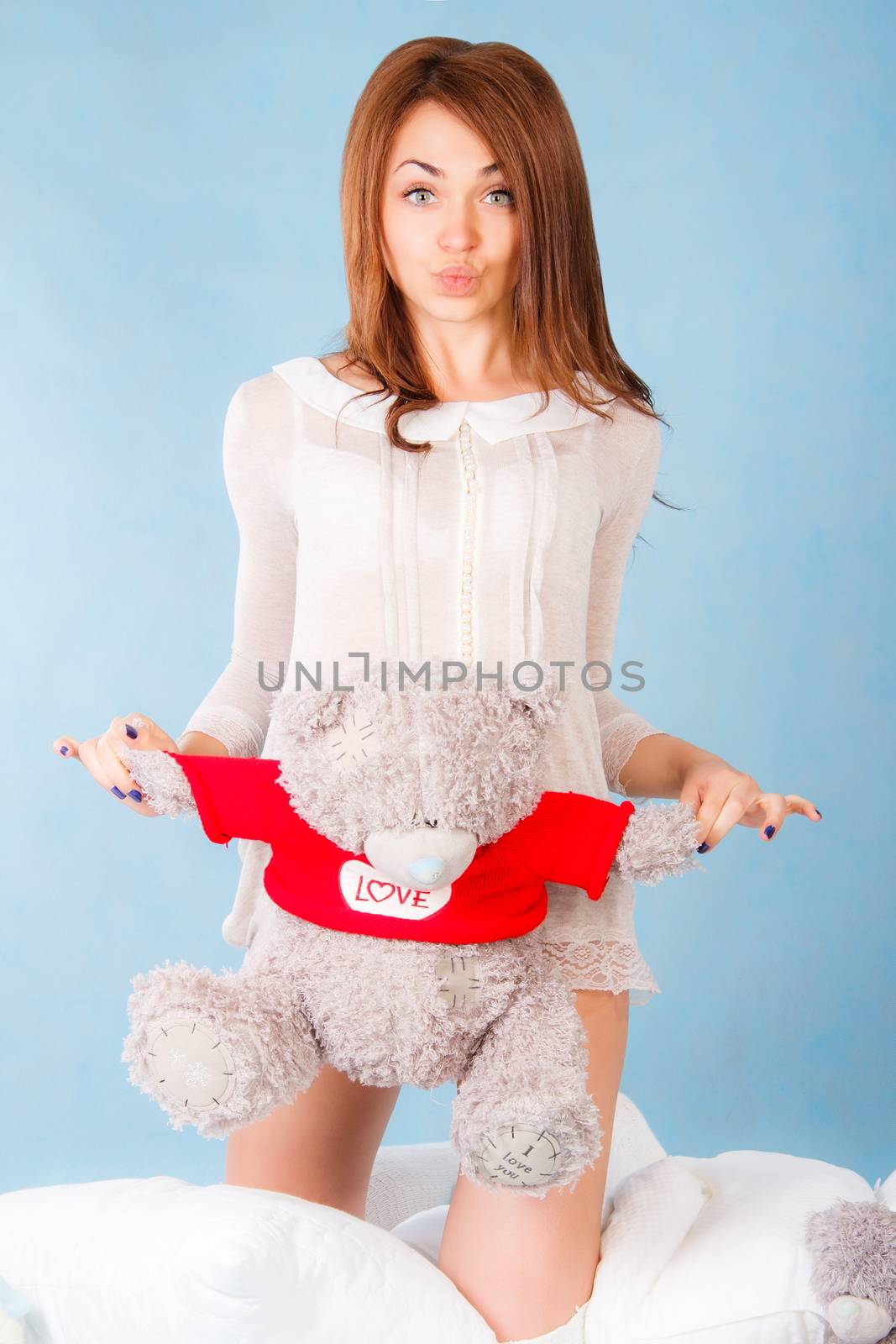 Cute young woman in a bed with a teddy bear over cyan background