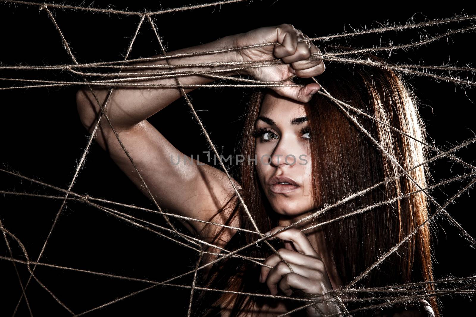 Beautiful young woman behind the interlaced ropes over black background
