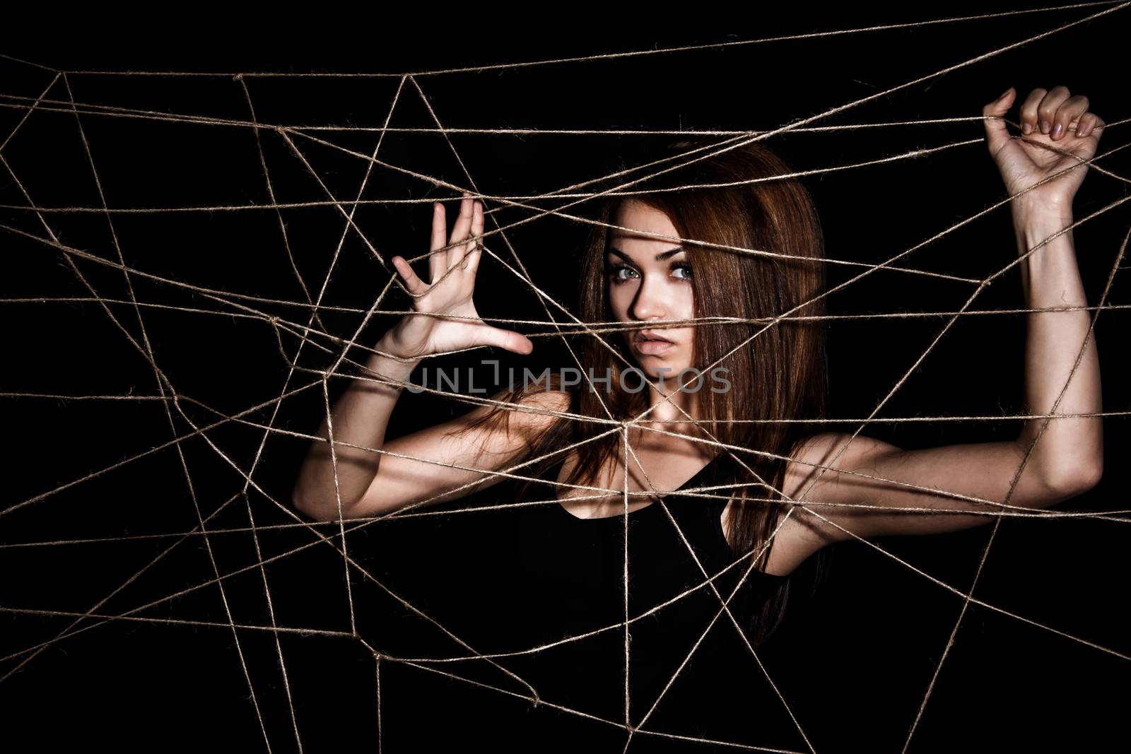 Beautiful young woman behind the net of ropes over black background