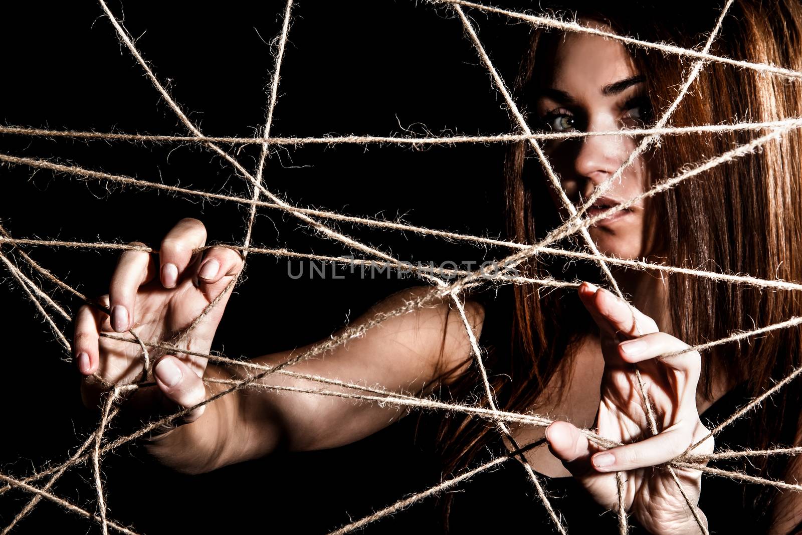 Beautiful young woman behind the net of ropes over black background