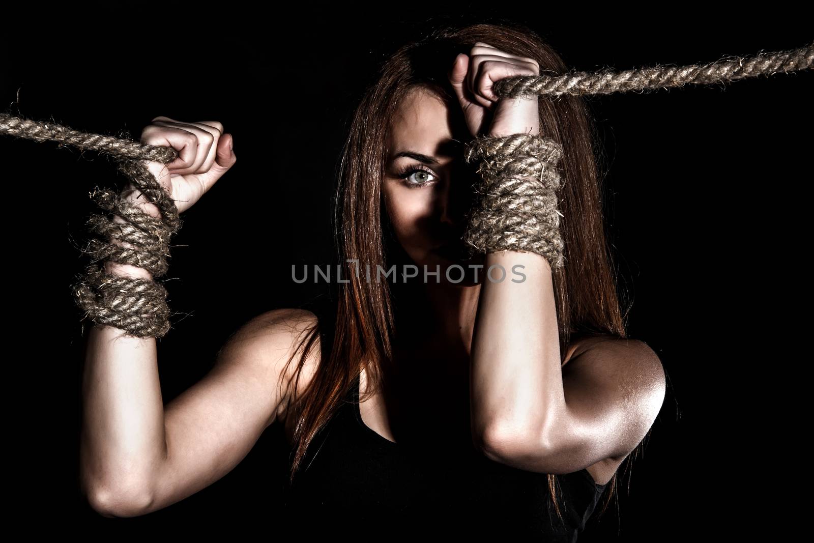 Beautiful young woman with tied arms over black background