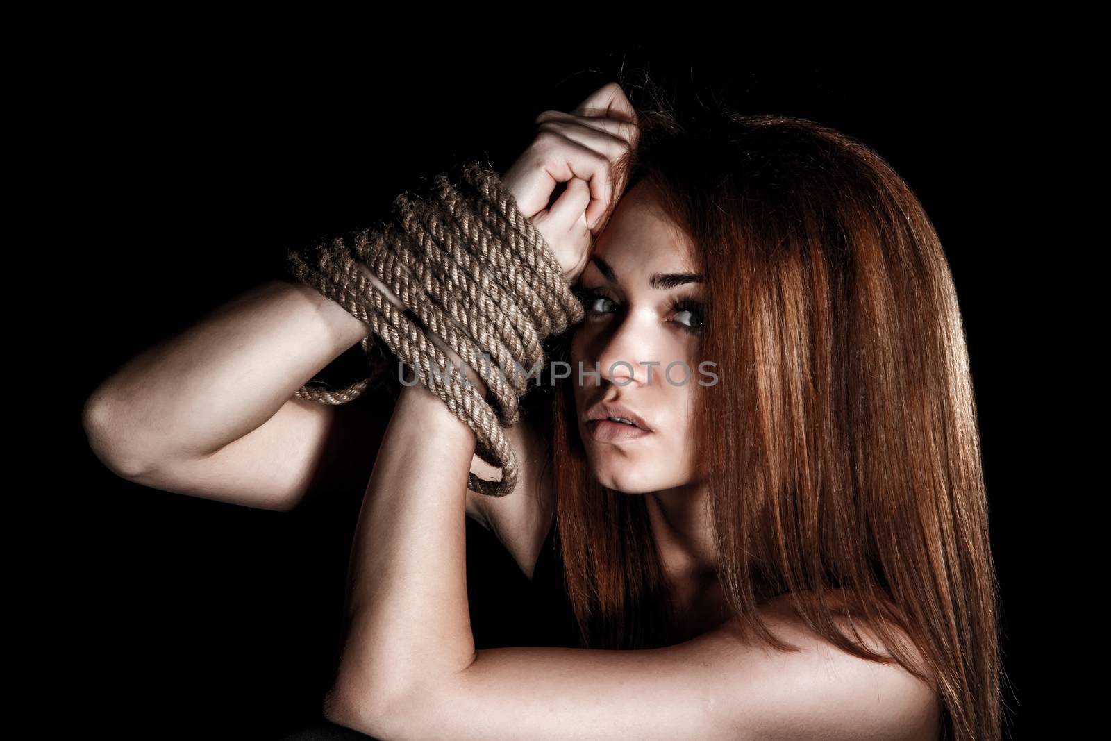 Beautiful young woman with tied arms over black background