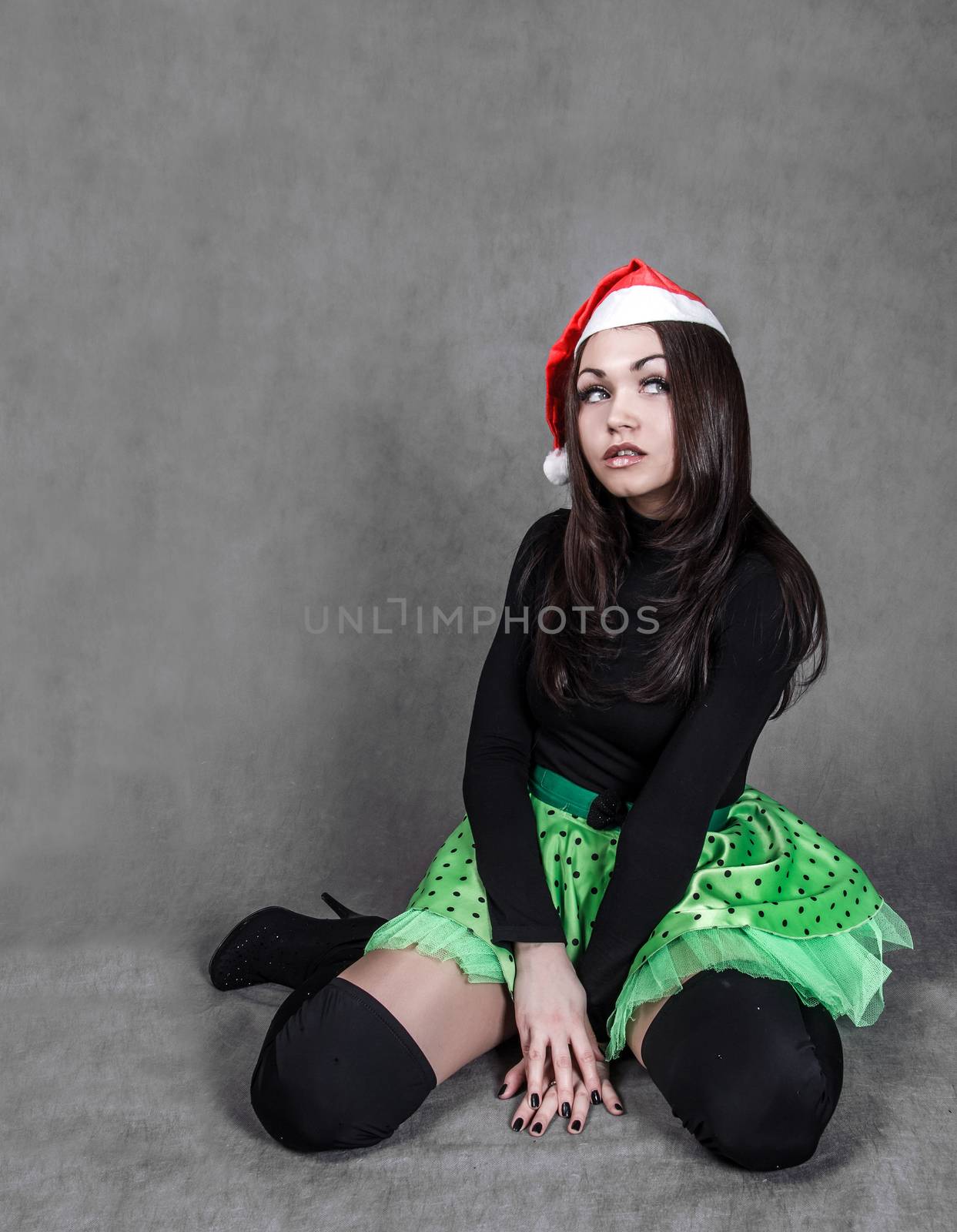 Young attractive woman in a bright green skirt and Christmas hat over grey background