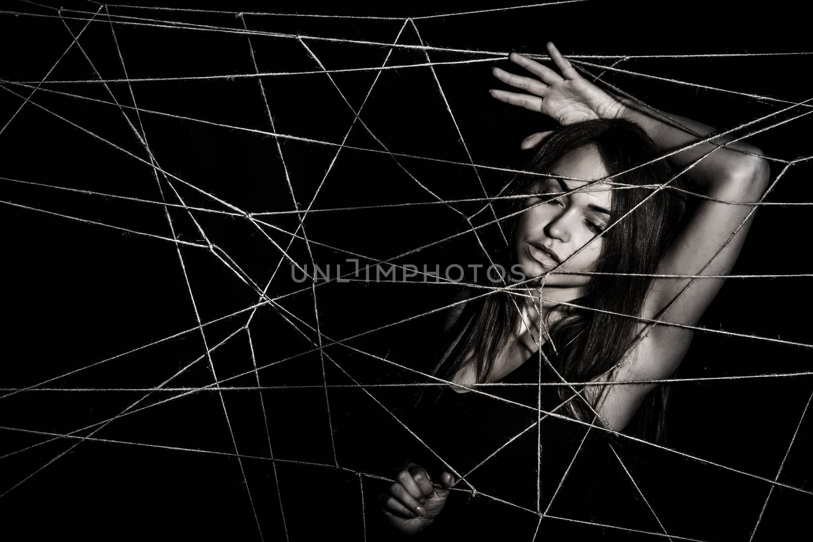 Young woman entangled the net of ropes over black background