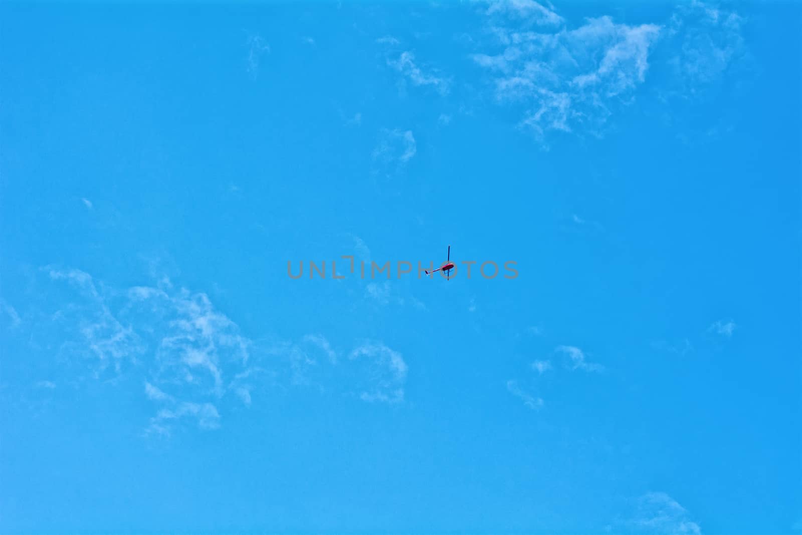 Small red helicopter hovering on blue sky