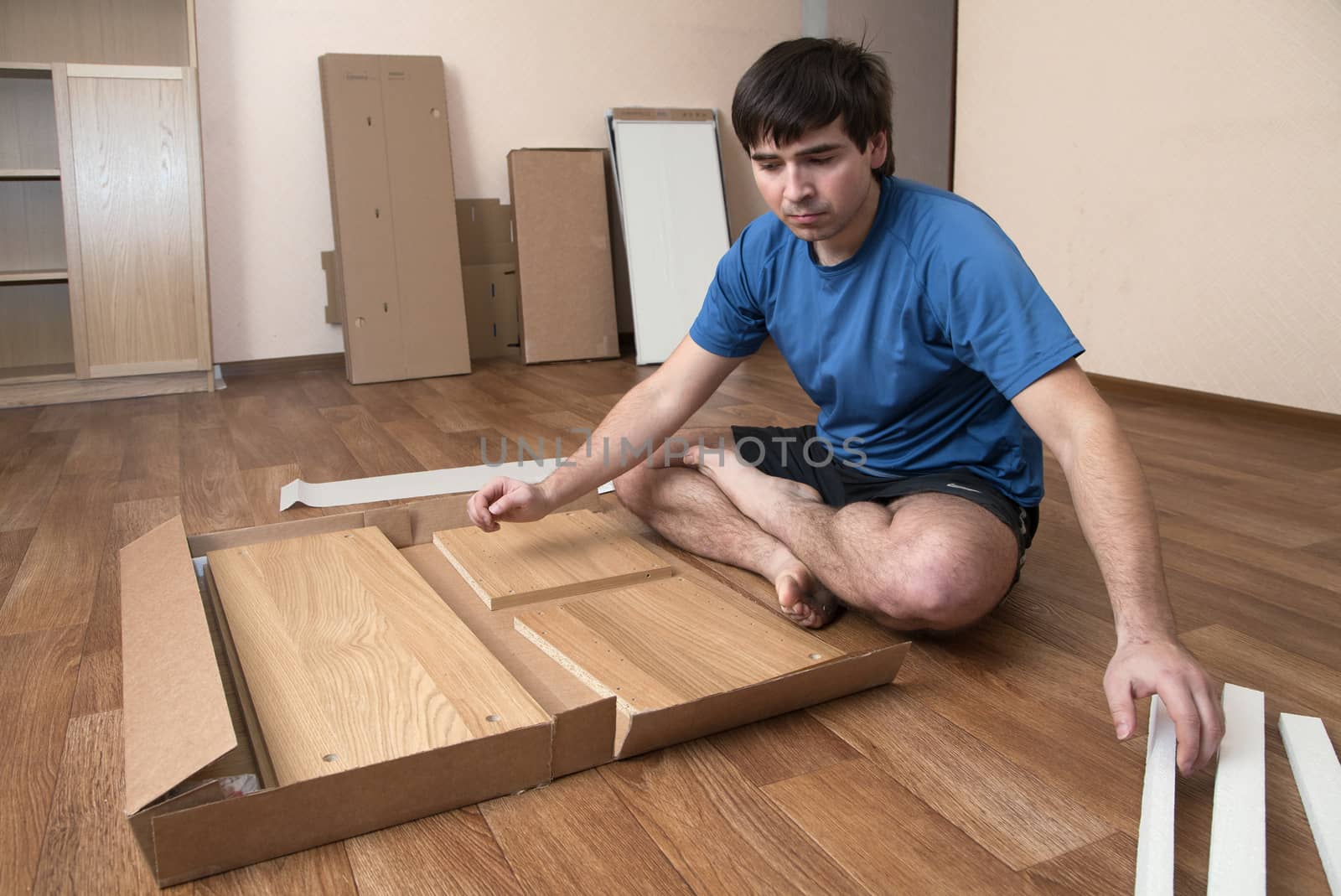 Young man sitting on floor assembling flatpack closet