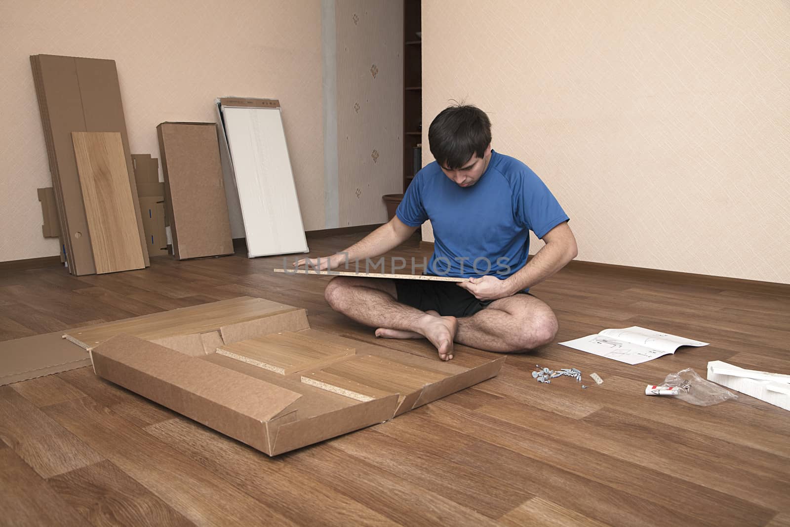 Young man sitting on floor assembling flatpack closet