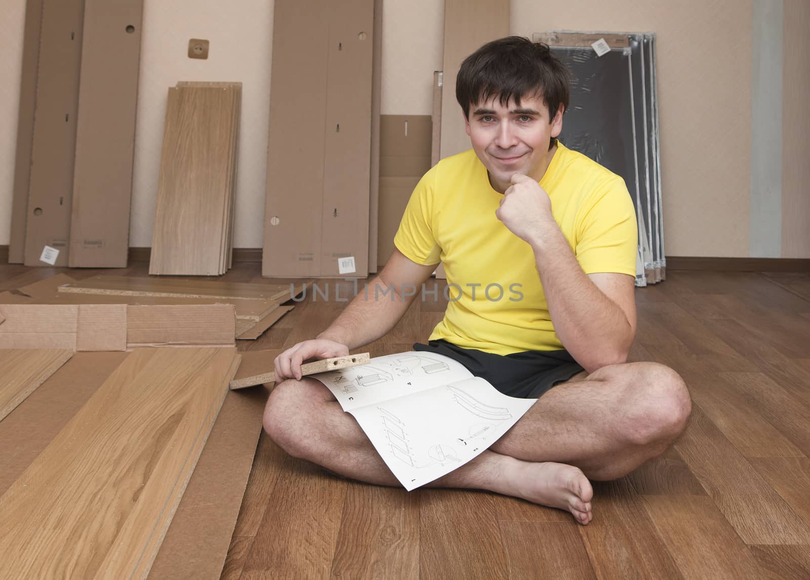 Young man sitting on floor assembling flatpack closet