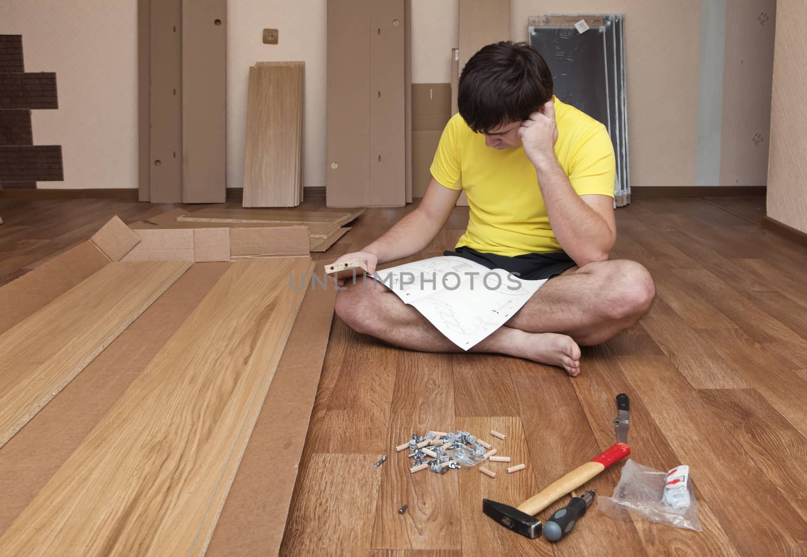 Young man sitting on floor assembling flatpack closet