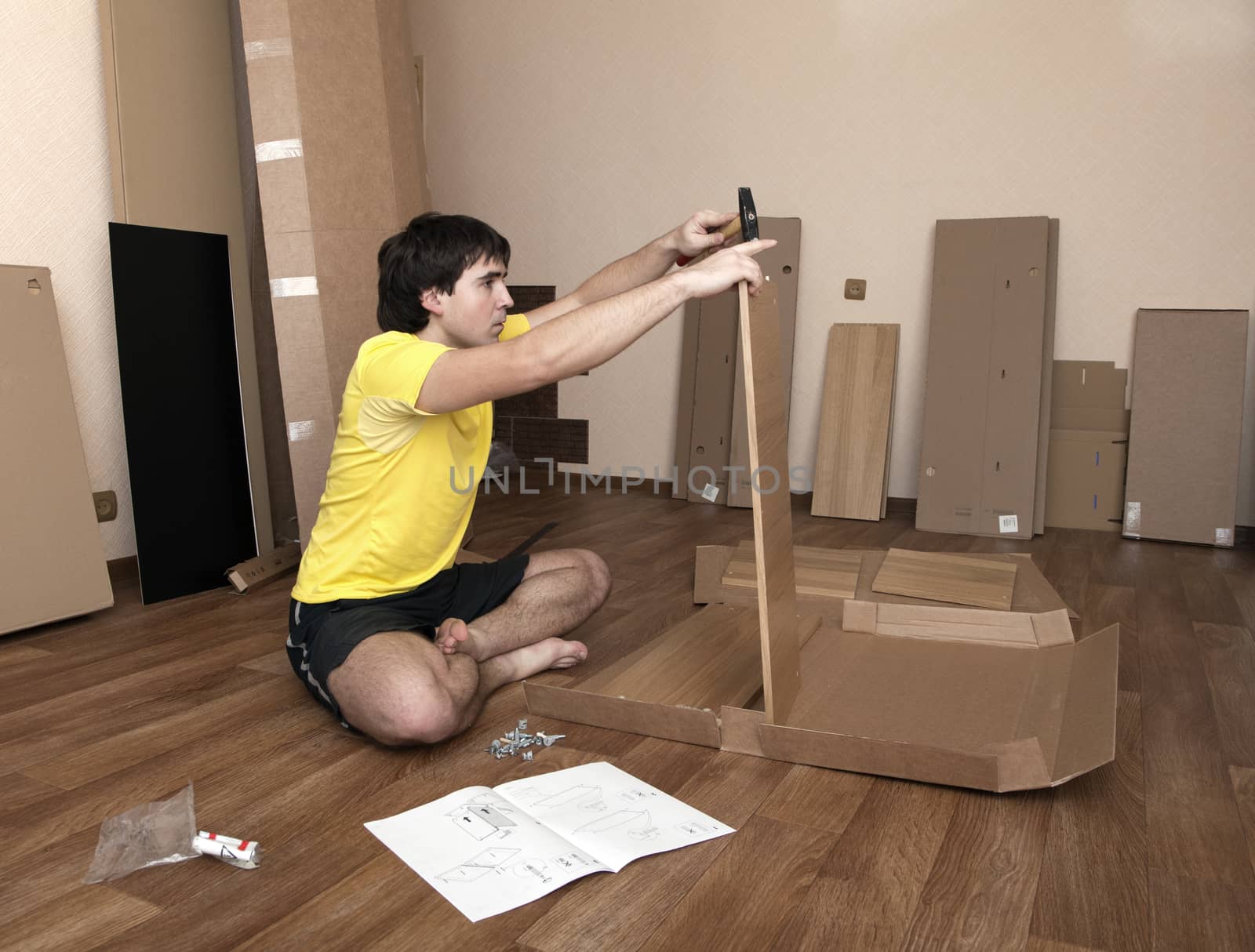 Young man sitting on floor assembling flatpack closet