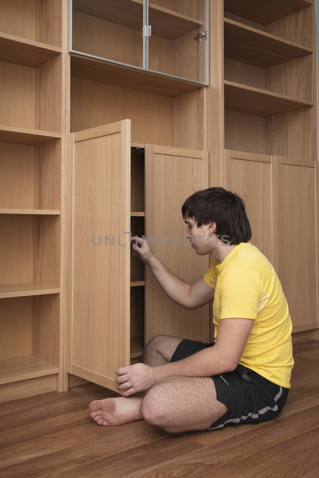 Young man sitting on floor assembling flatpack closet