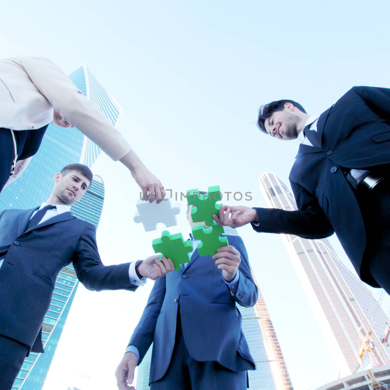 Business people assembling jigsaw puzzle near skyscrapers