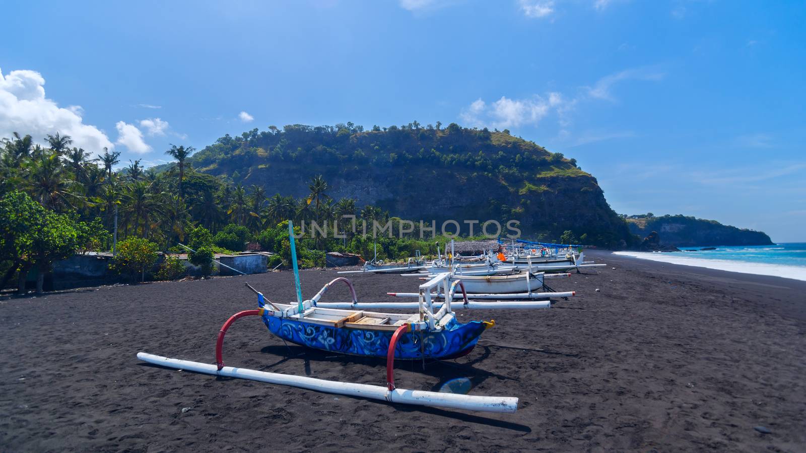 Junk on the beach of black sand on the island of Bali in Indonesia. Summer sunny day.