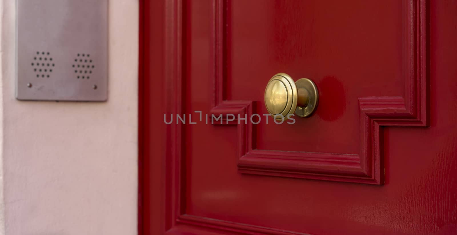 Shiny brass metal doorknob on red wooden entrance door