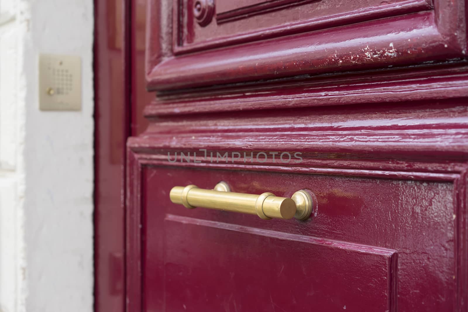 Old brass door handle on sturdy old textured maroon red wooden door