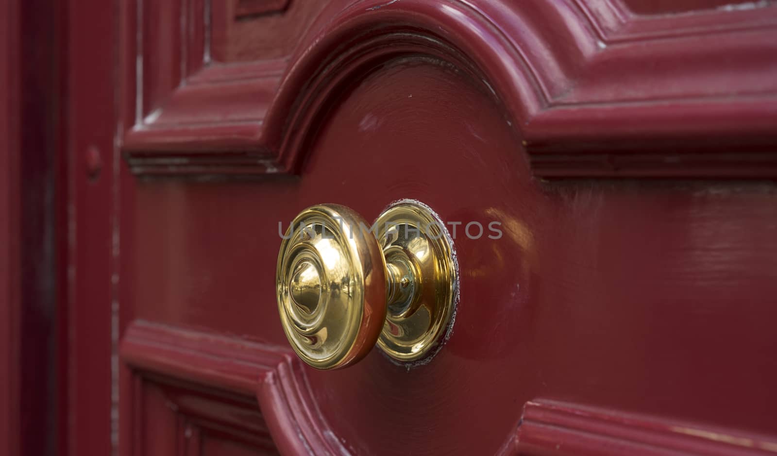 Shiny brass metal doorknob on maroon red wooden entrance door, secure entry to house