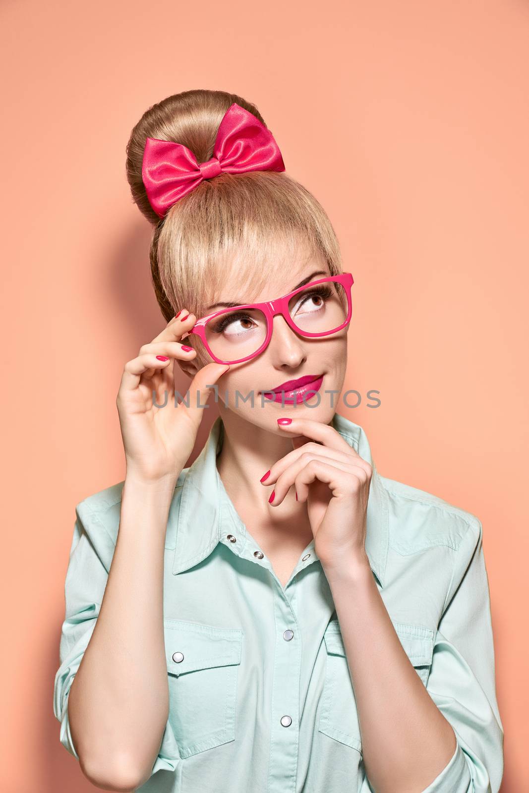 Beauty fashion nerdy woman in stylish glasses thinking, idea. Attractive pretty funny blonde girl smiling. Confidence, success, Pinup hairstyle bow makeup. Unusual playful, expression.Vintage, on pink