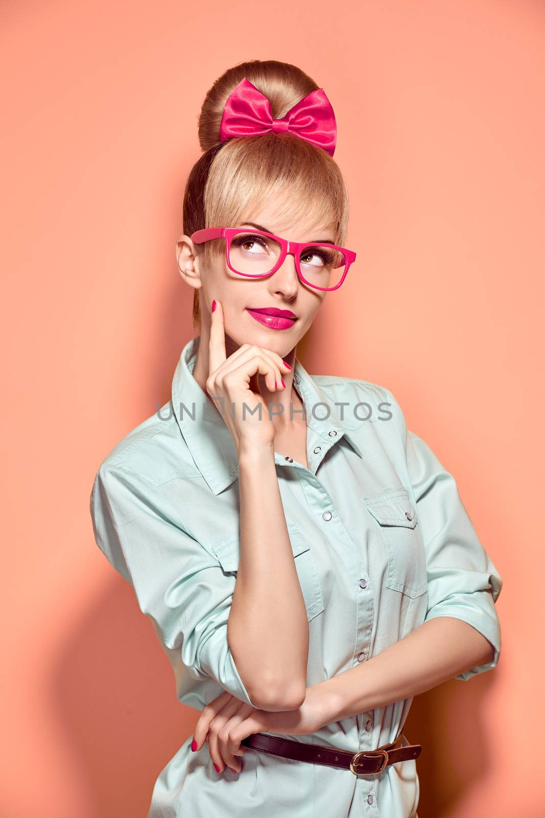 Beauty fashion nerdy woman in stylish glasses thinking, idea. Attractive pretty funny blonde girl smiling. Confidence, success, Pinup hairstyle bow makeup. Unusual playful, expression.Vintage, on pink