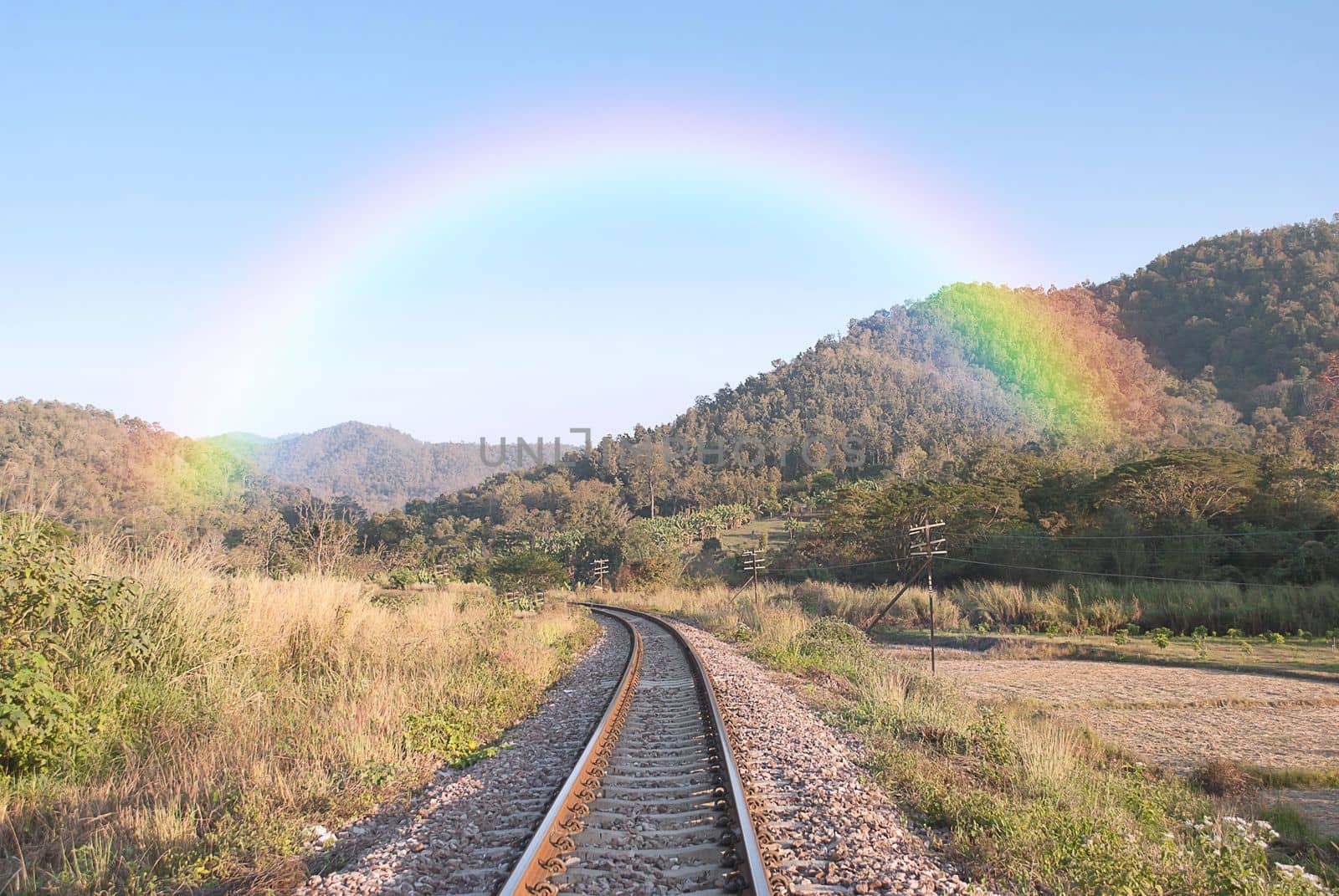 railroad rails with rainbow in to the mountain