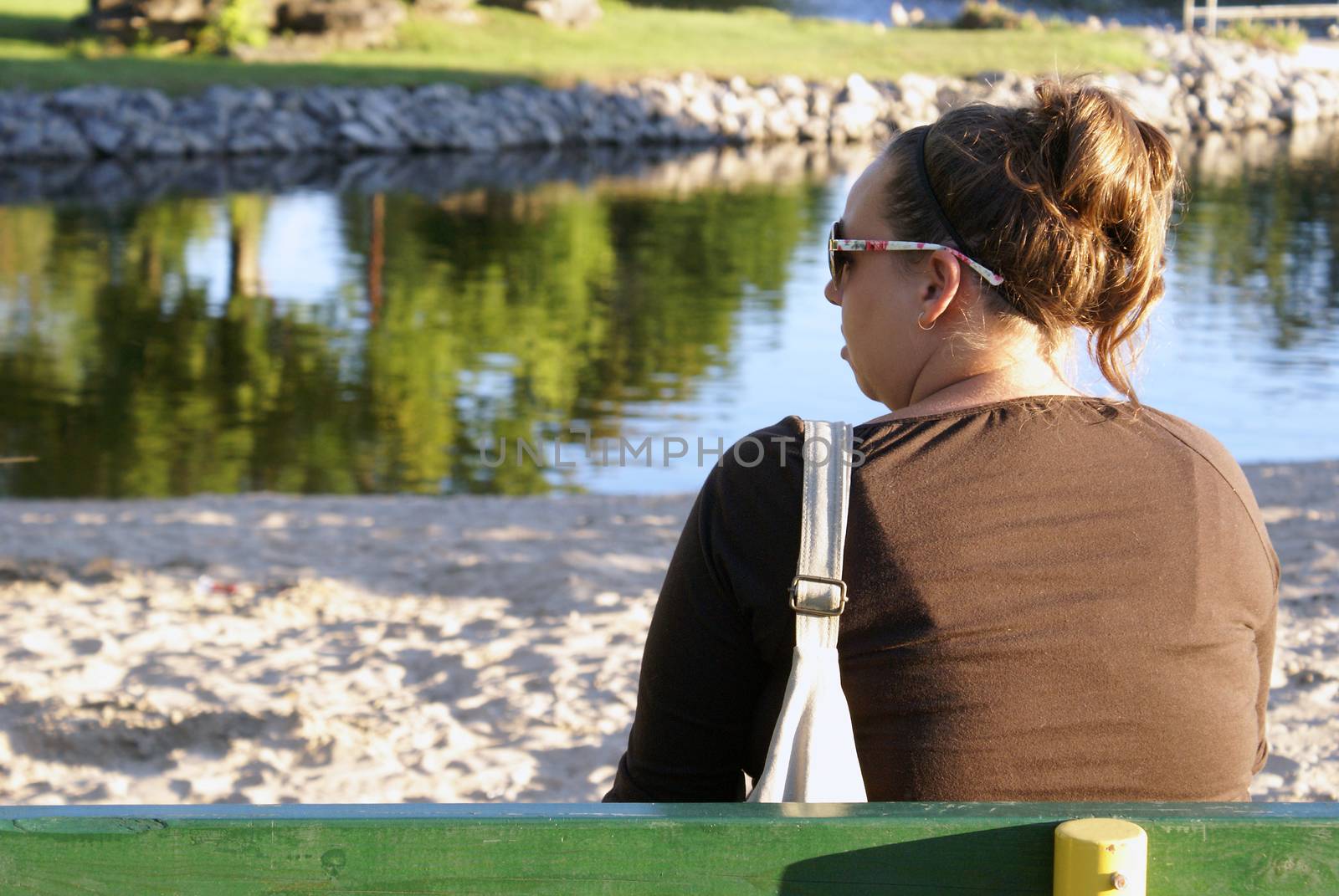 A woman sits on a bench for some leisure time near the water.