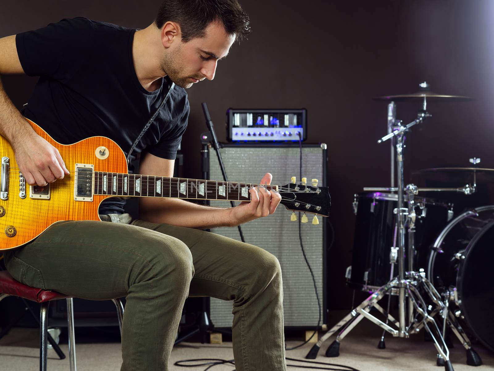 Photo of a man in his late 20's sitting on stage playing guitar.