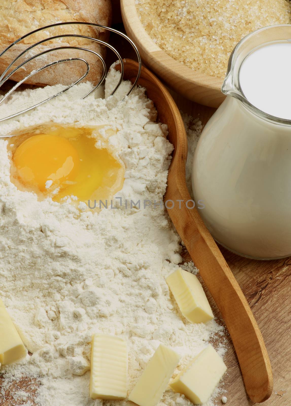 Preparing Homemade Dough with Ingredients, Wooden Spoon and Egg Whisk closeup on Wooden Cutting Board