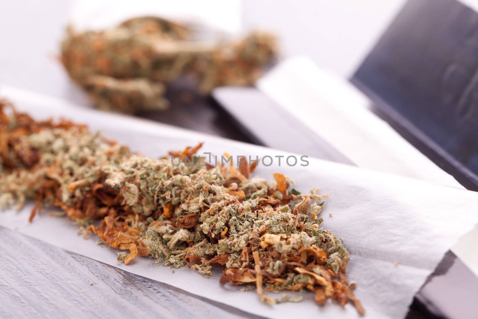 Close up Dried Cannabis Leaves on a Resealable Cellophane Wrapper and a Rolling Paper with Filter on Top of the Table