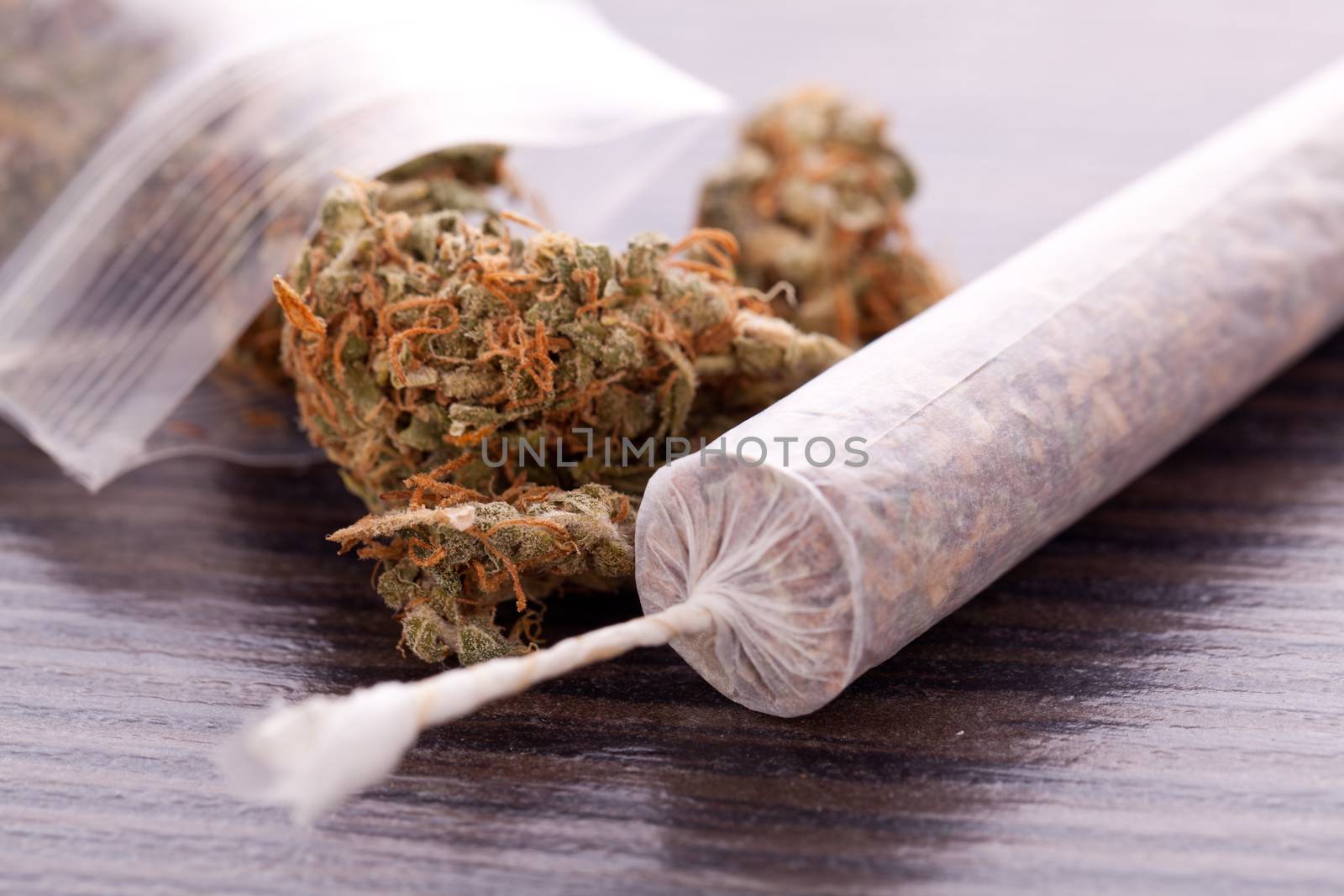 Close up of dried marijuana leaves and tied end of marijuana joint with translucent rolling paper on white background