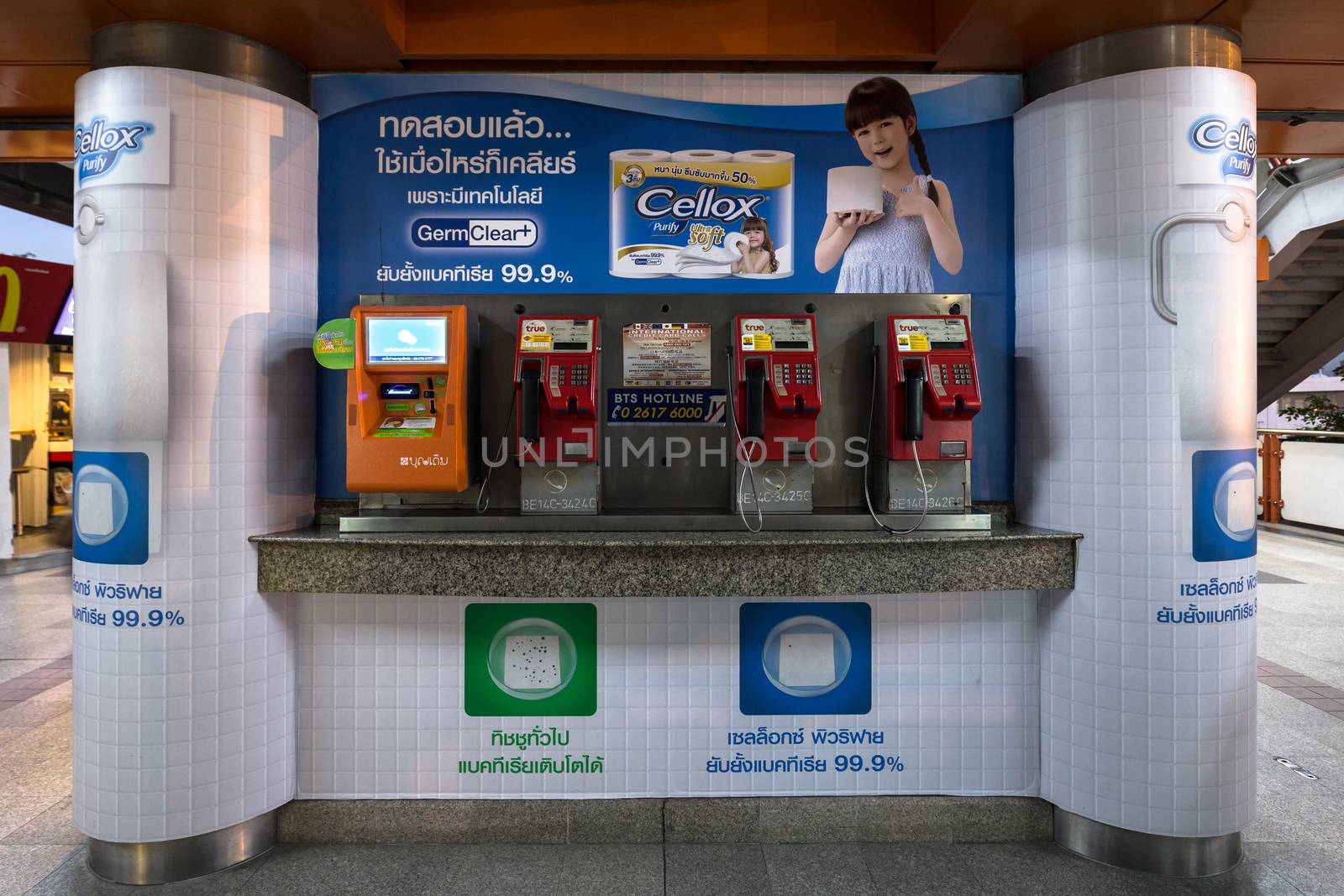 Bangkok, Thailand - January 18, 2016 : public payphone and top up machine on the corner with advertisement poster in Thai language in the background at BTS Mo Chit station in the evening