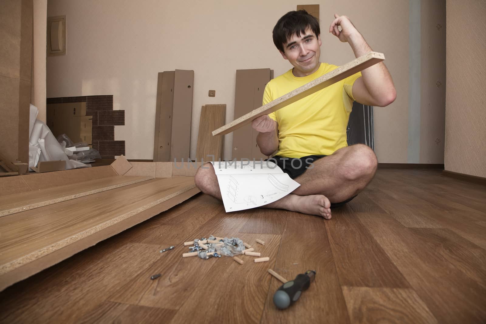 Young man sitting on floor assembling flatpack closet