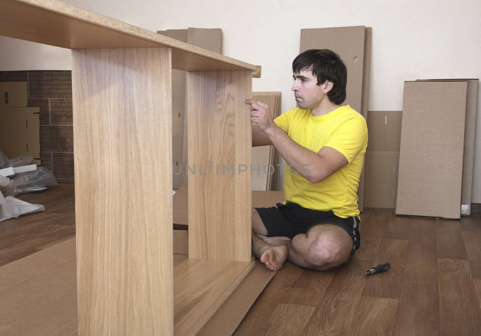 Young man sitting on floor assembling flatpack closet