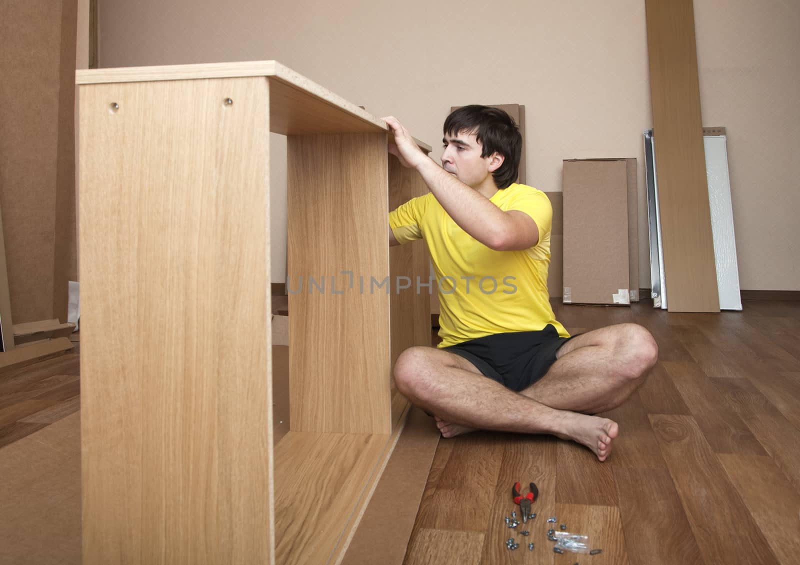 Young man sitting on floor assembling flatpack closet