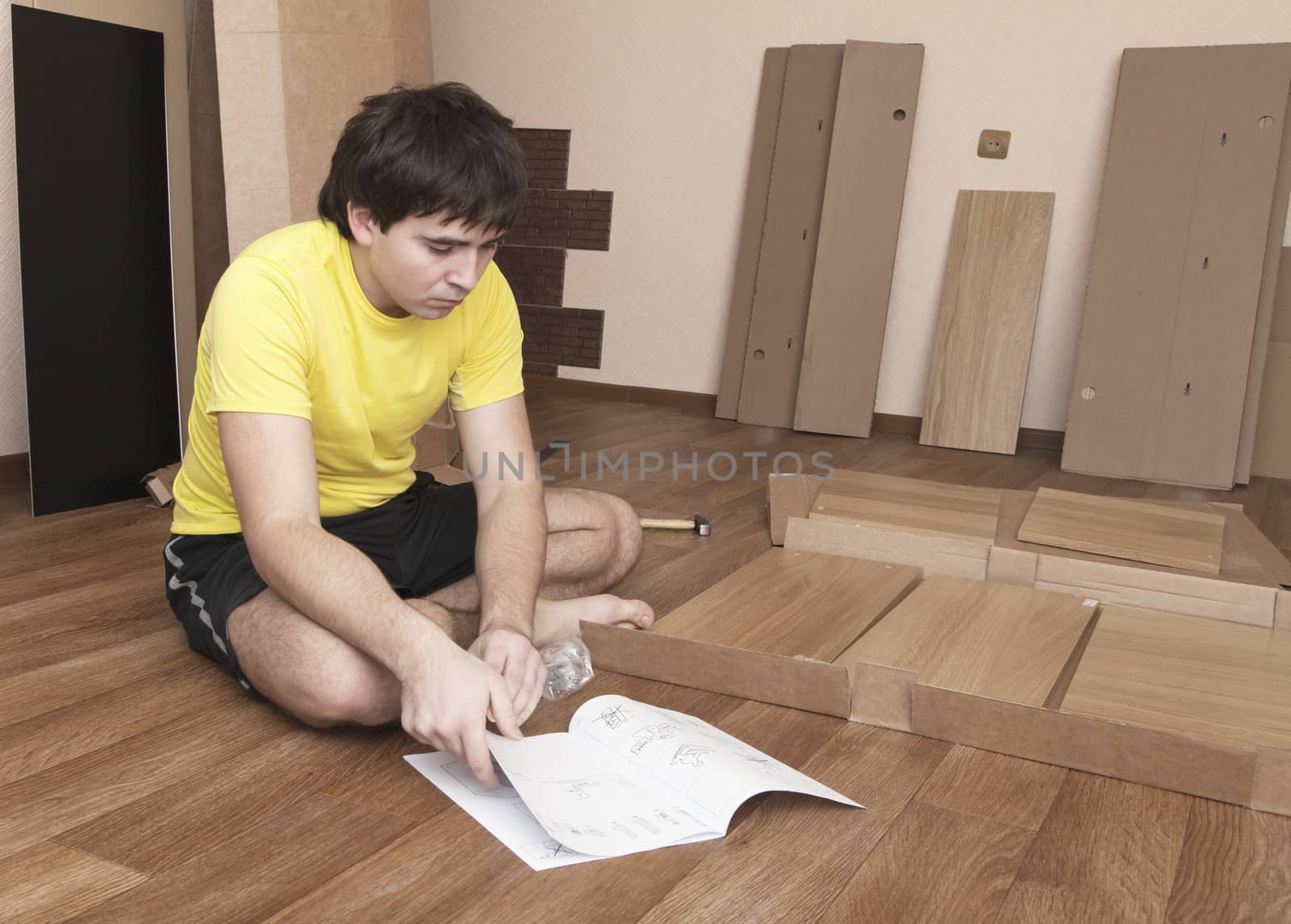 Young man sitting on floor assembling flatpack closet