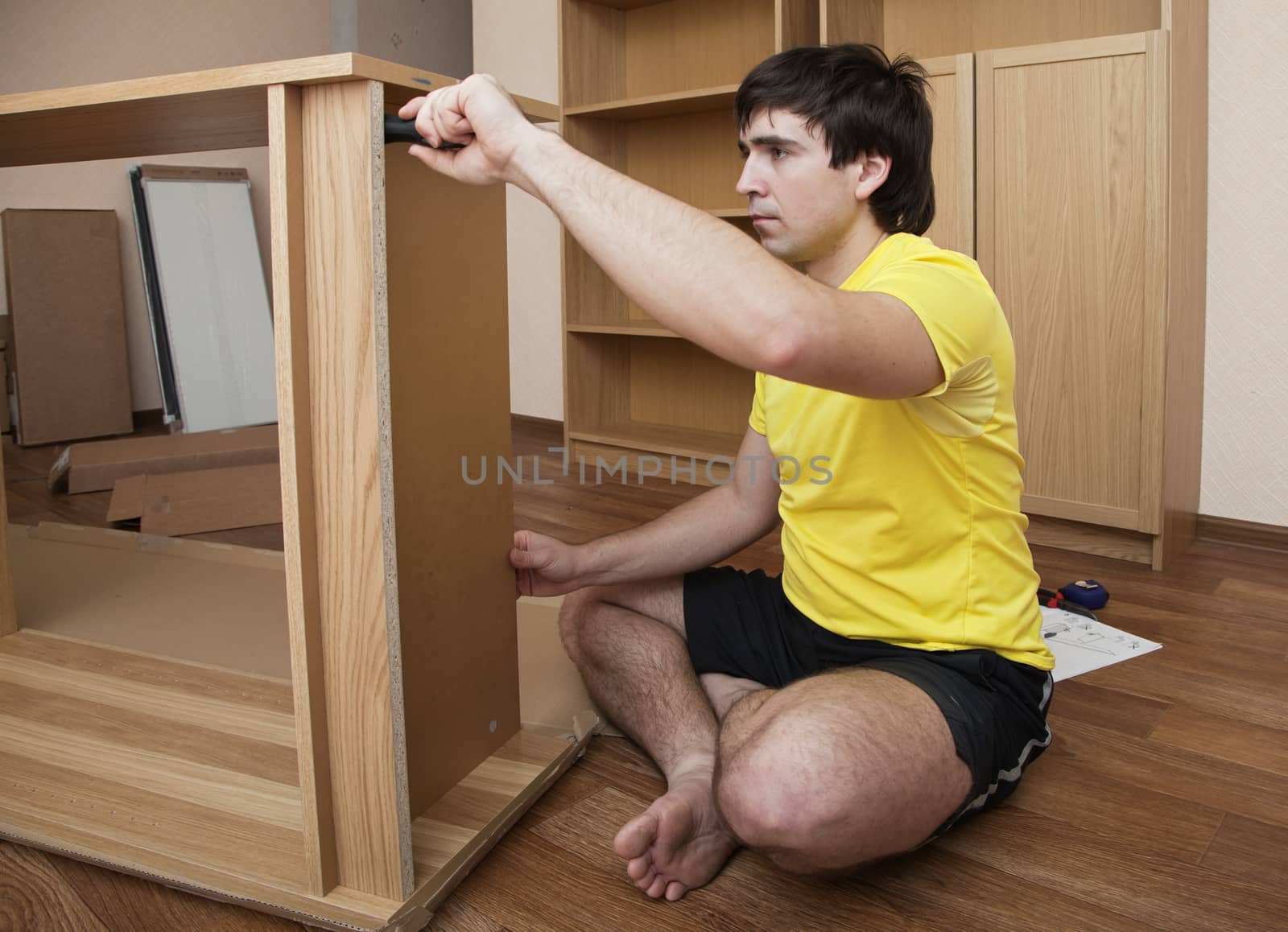 Young man sitting on floor assembling flatpack closet