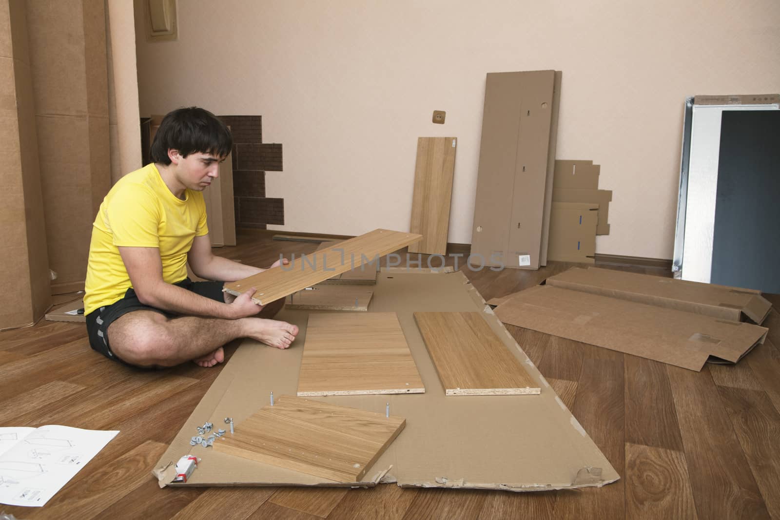 Young man sitting on floor assembling flatpack closet