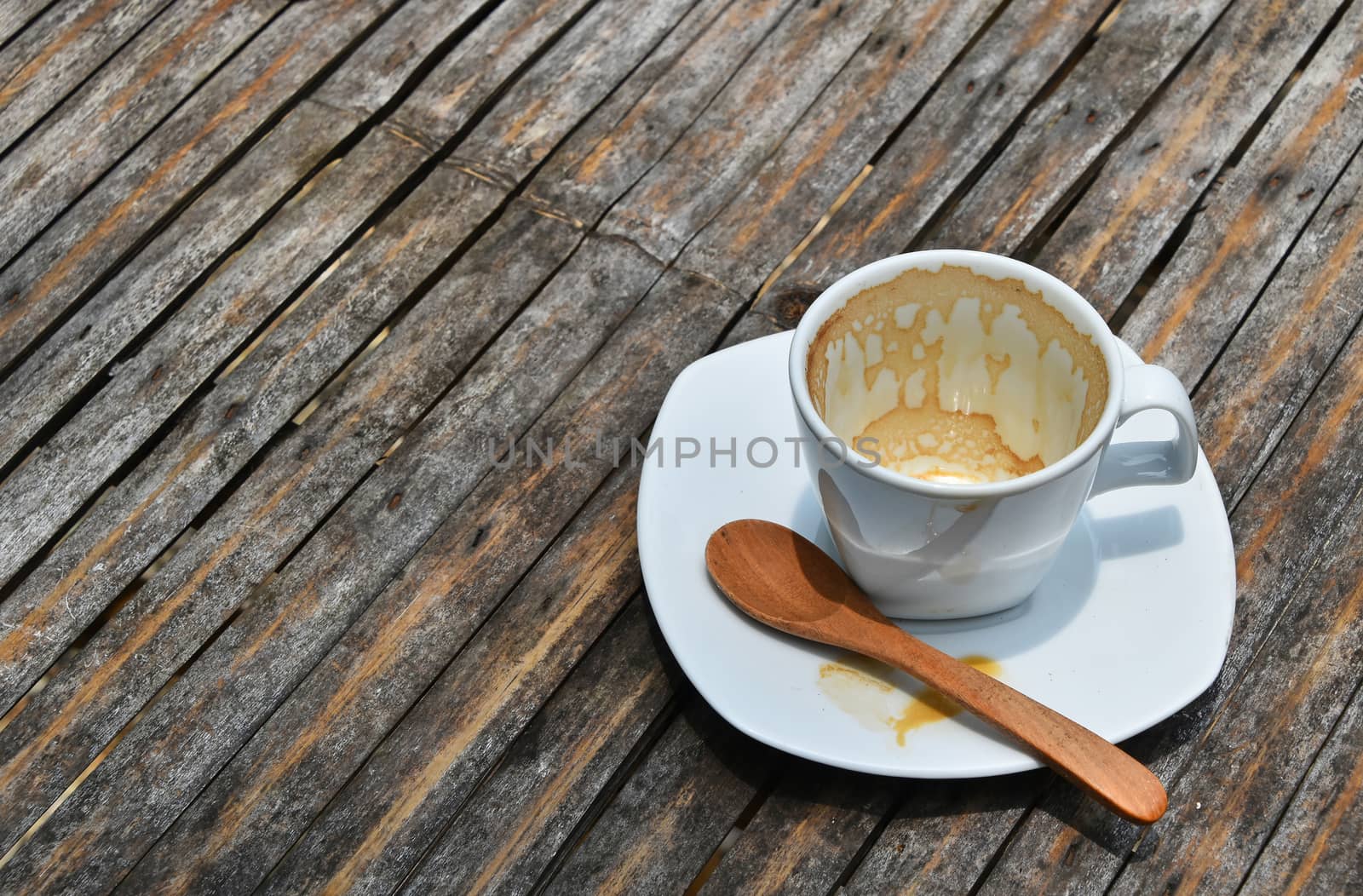 One overdrunk finished white cup of espresso coffee on porcelain saucer with wooden spoon on old vintage bamboo table