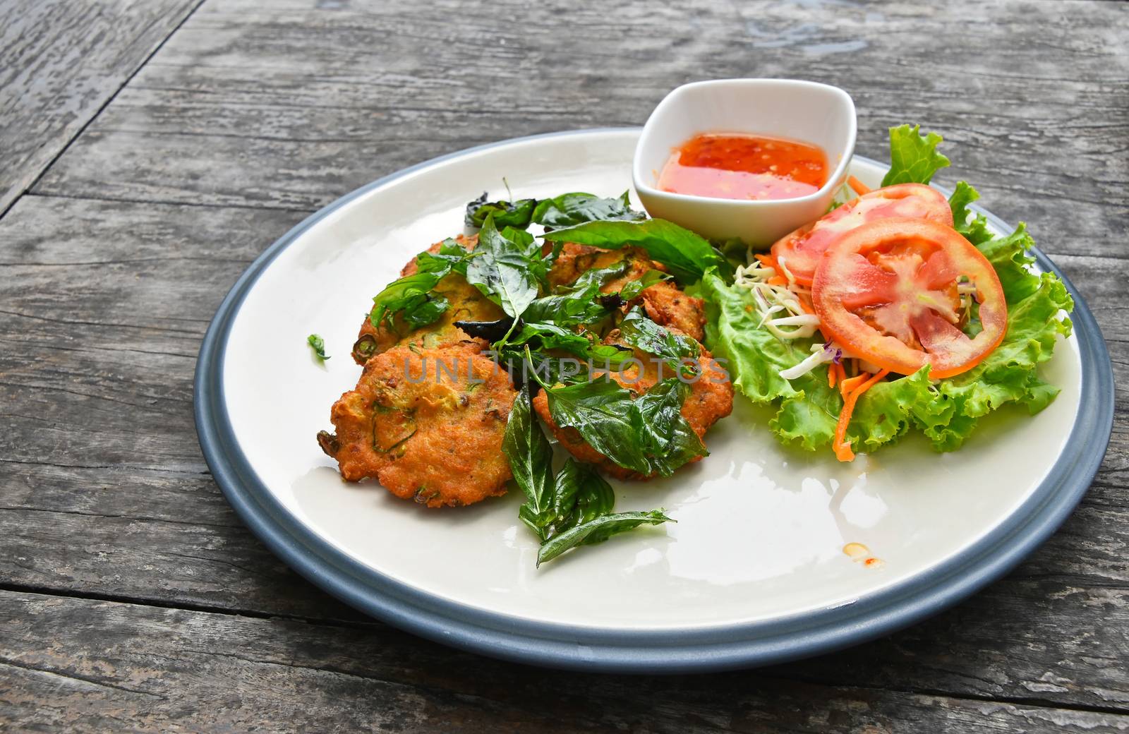 Plate of fish and shrimp deep fried cakes croquettes snack with salad basil leaves and hot sauce on vintage wooden table surface