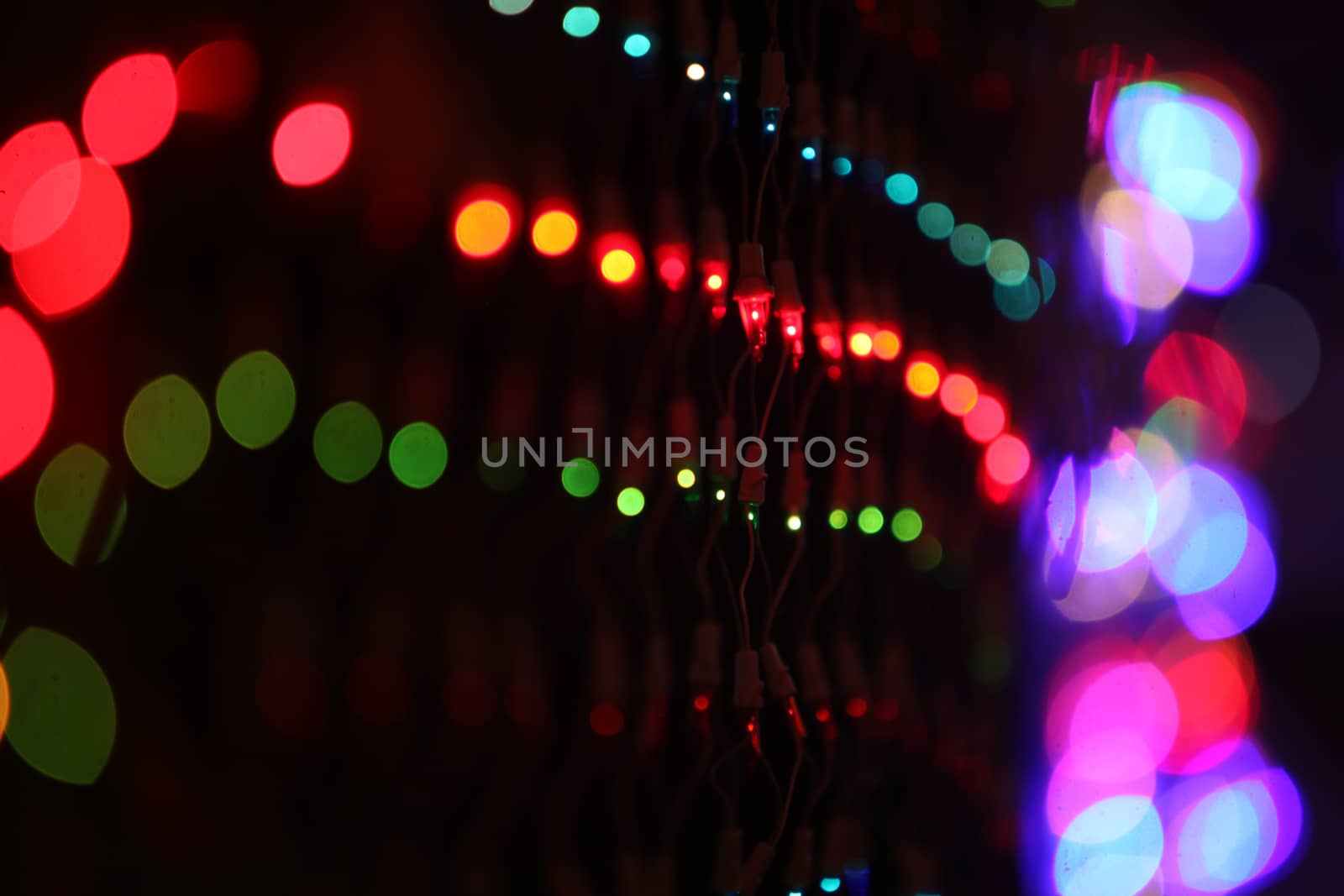 A background with a view of colorful wire mesh, on the backdrop of blur colorful lights during a festival.