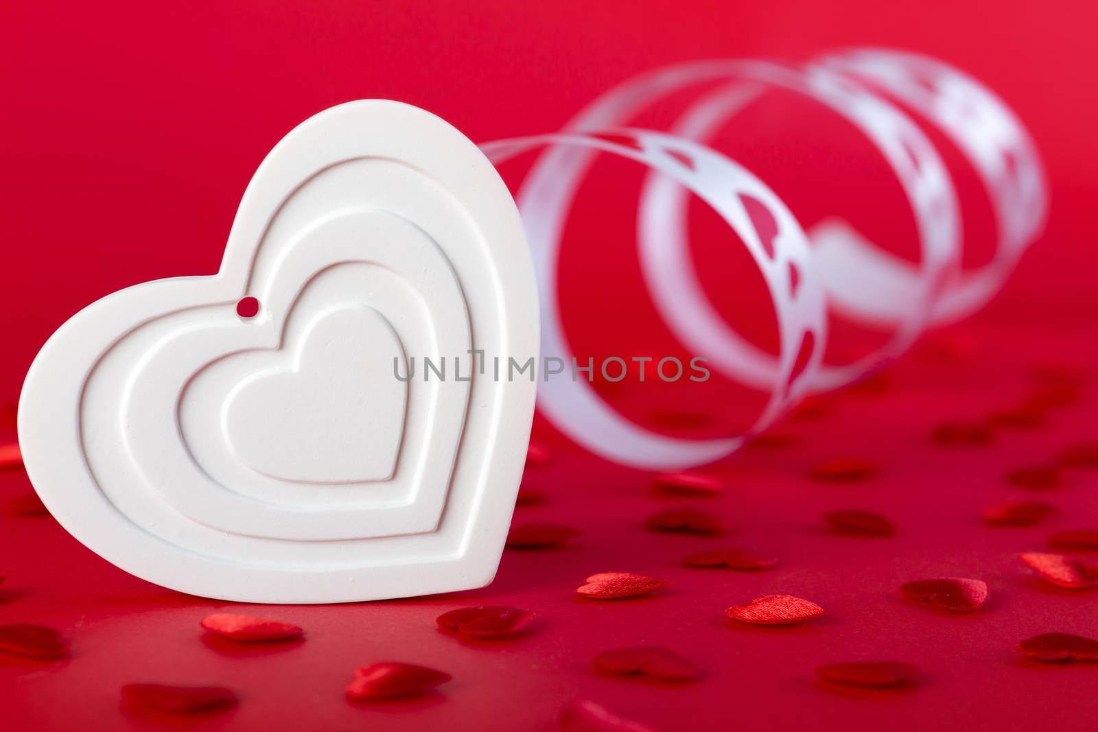 white shape heart with ribbon and red hearts on red background. Valentines day concept.
