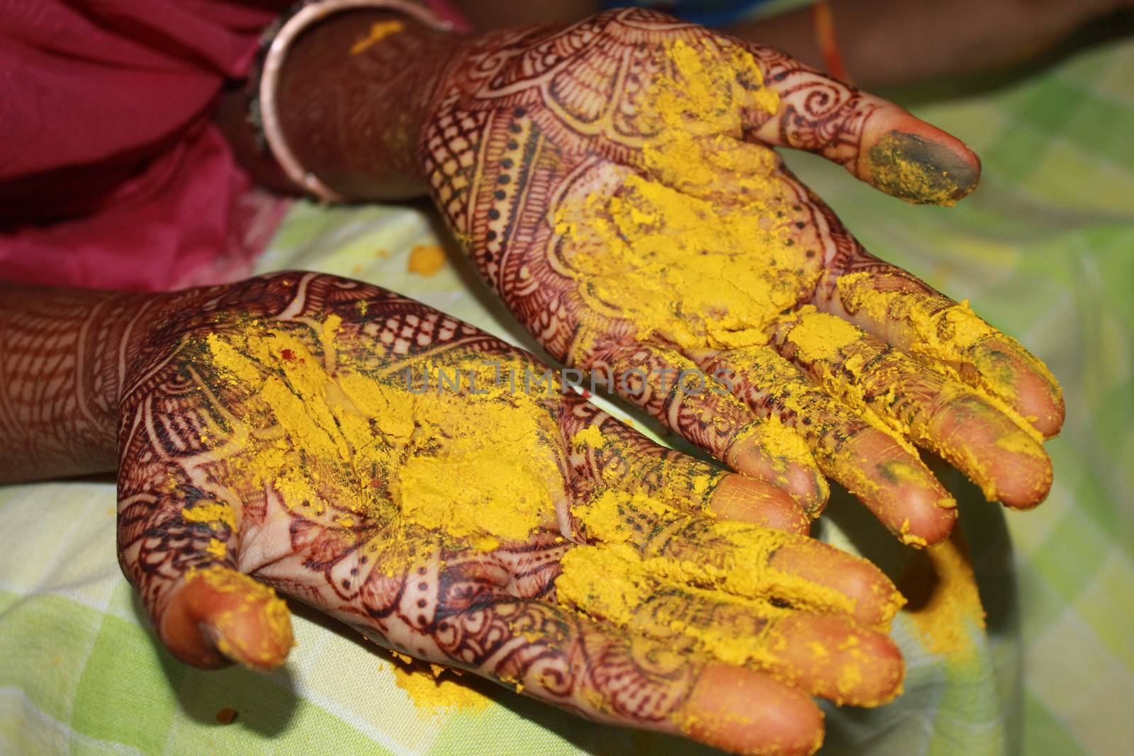 A view of hands with mehendi having turmeric / haldi on their hands as a part of a traditional wedding ritual in India.