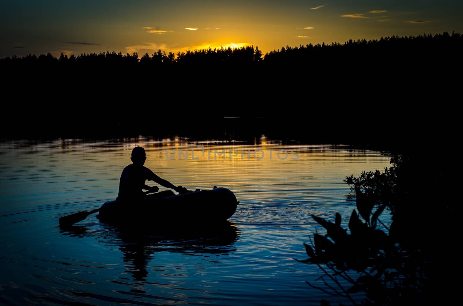 A fisherman floating on a boat on the lake at sunset
