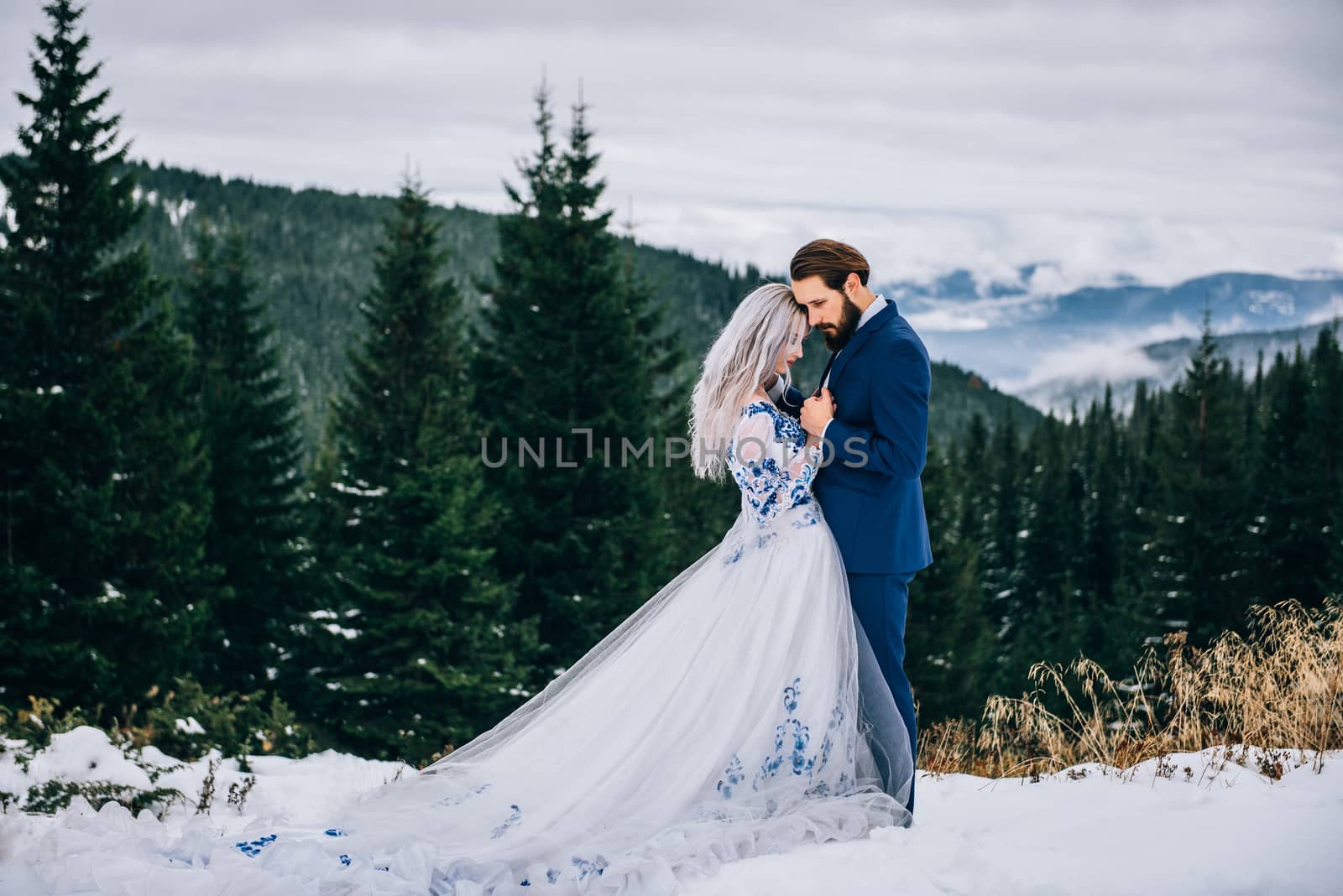 groom in a blue suit and bride in white, embroidered with blue pattern, dress on a background of green pine forests in the mountains of the Carpathians