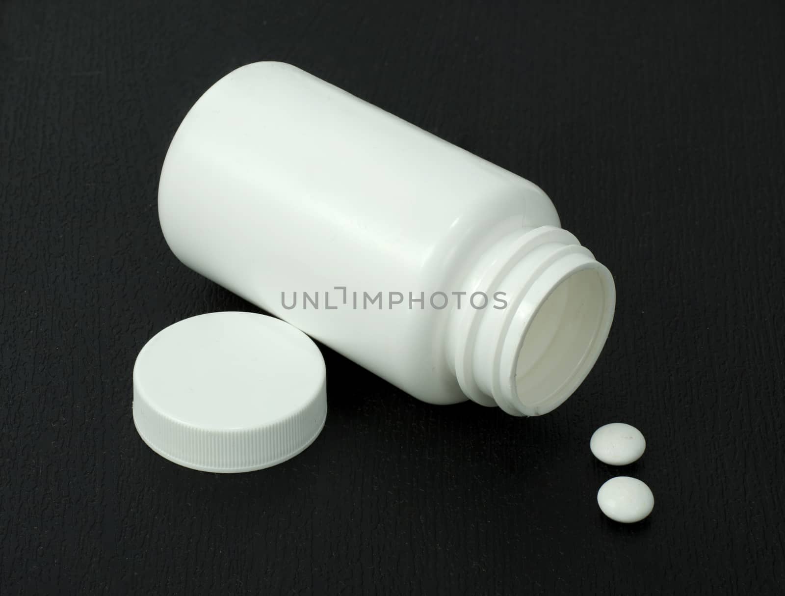 two white pills with white jar on a dark background